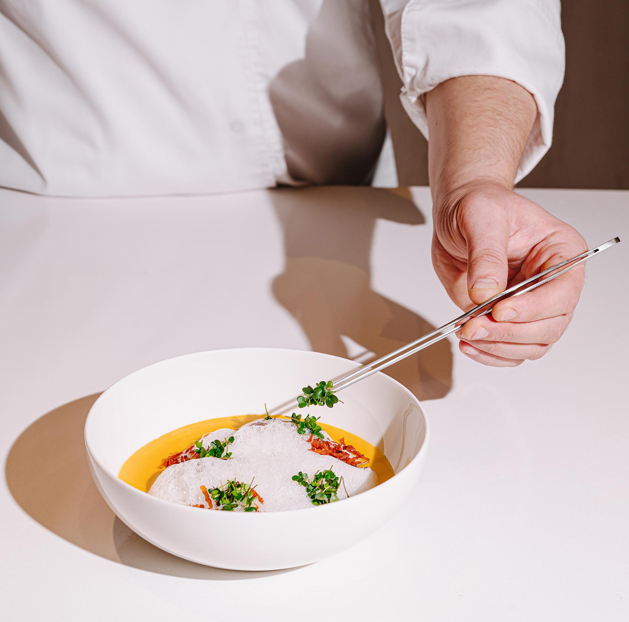 Chef arranging plated seasonal dish on a dark table
